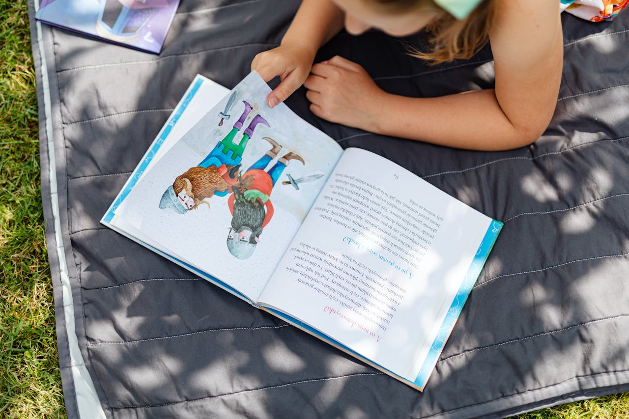 why-choose-us A young girl enjoys reading on a blanket in the sunlit outdoors, perfect summer relaxation.