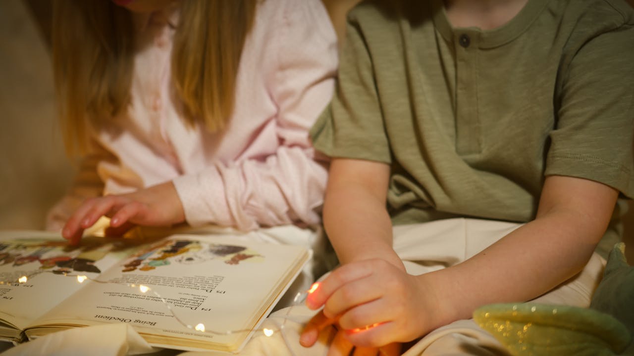 services-04 Two children reading a storybook under warm fairy lights, creating a cozy atmosphere.